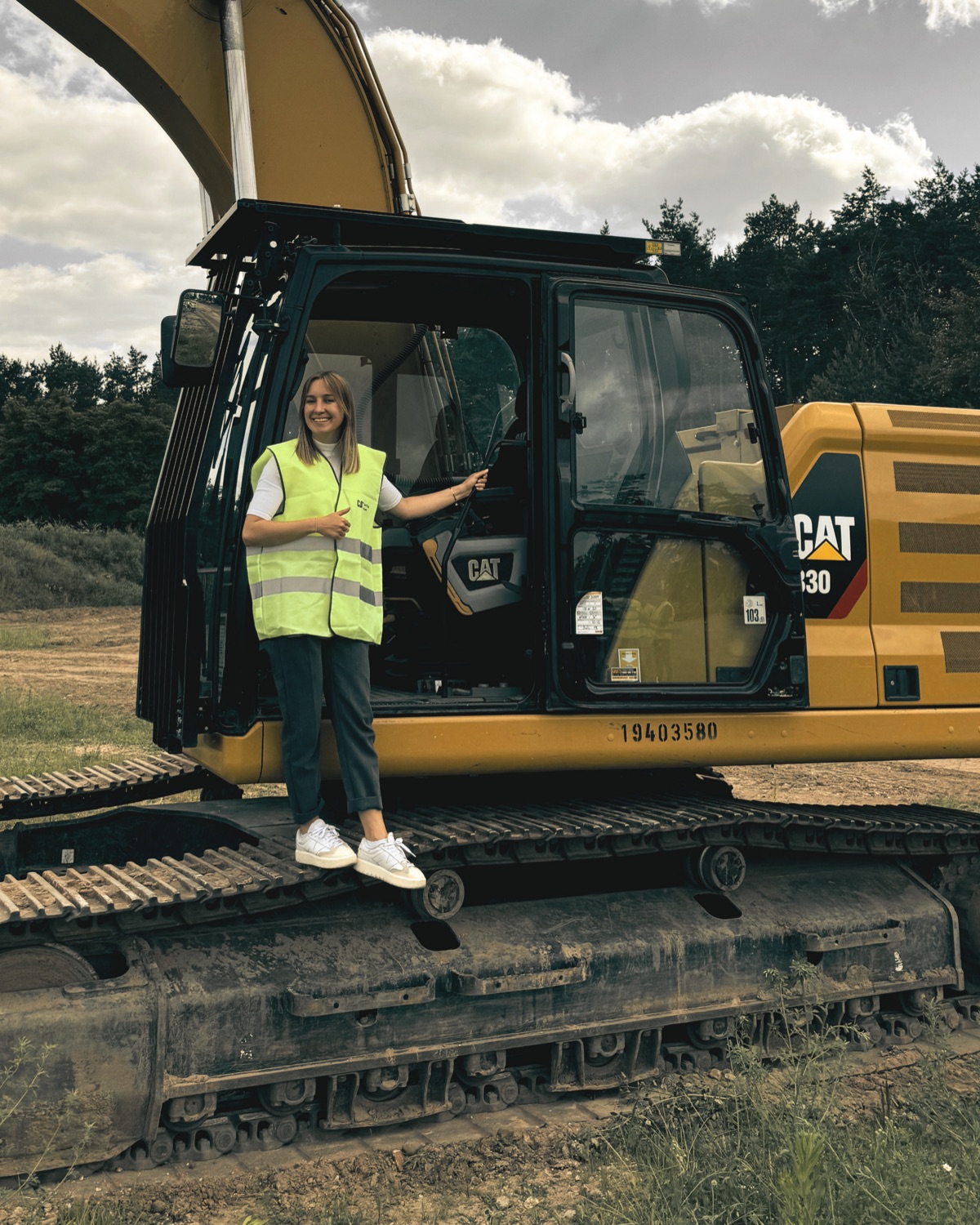 Julia Stein on site, standing on a CAT excavator